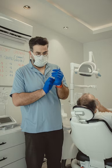 a dentist putting on blue gloves  and a patient lying on the dental chair